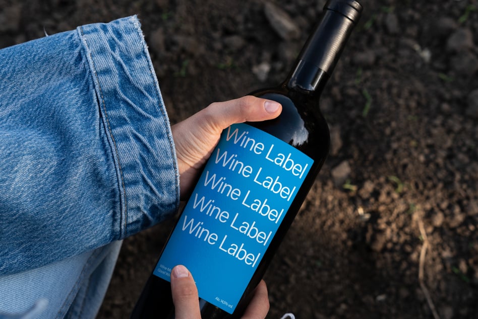 Hand holding wine bottle with blue label mockup on dirt ground