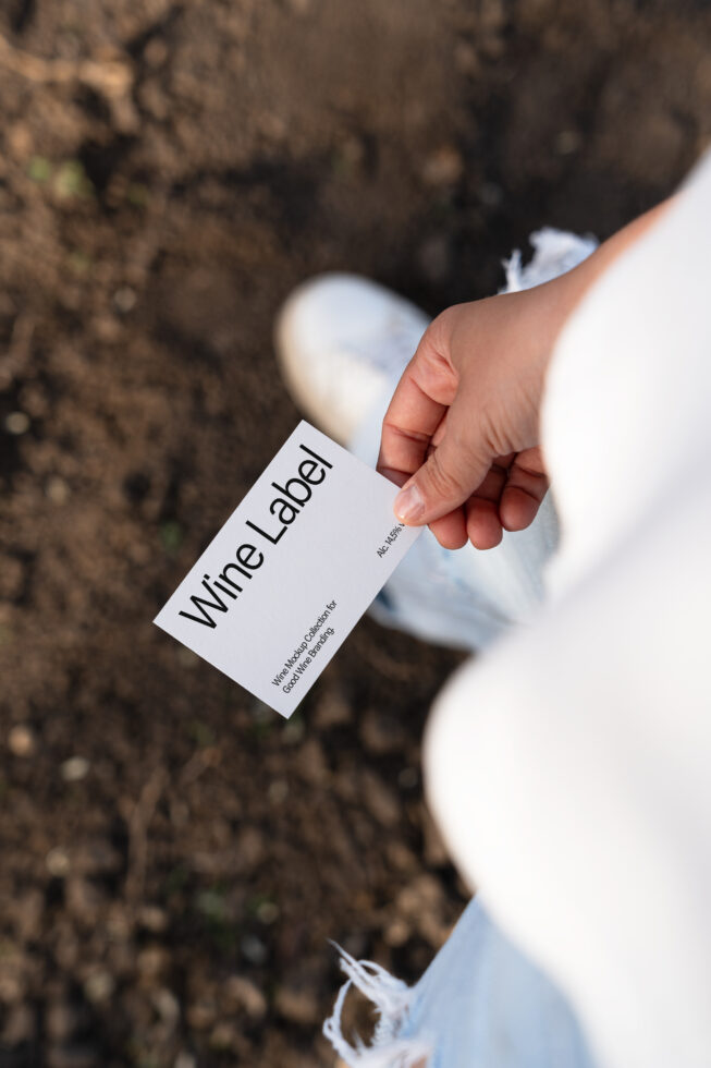 Hand holding a white wine label card outdoors, showcasing modern typography design. Perfect for branding mockups or design templates for creatives.