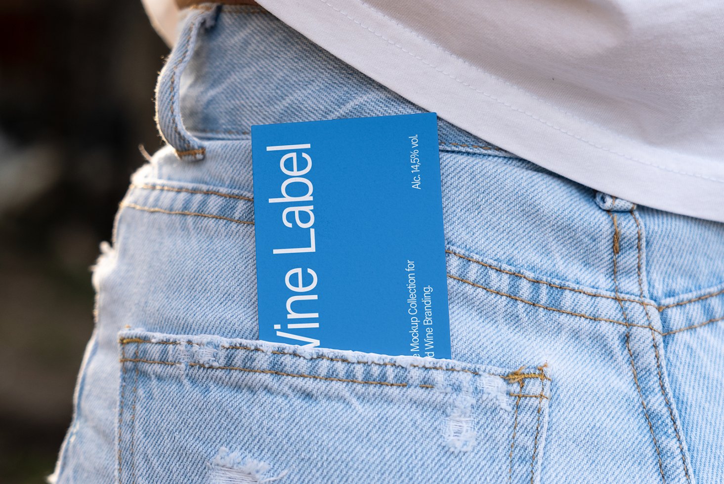 Mockup of blue wine label tucked in pocket of ripped jeans; ideal for digital designers in need of realistic graphic templates or branding assets.