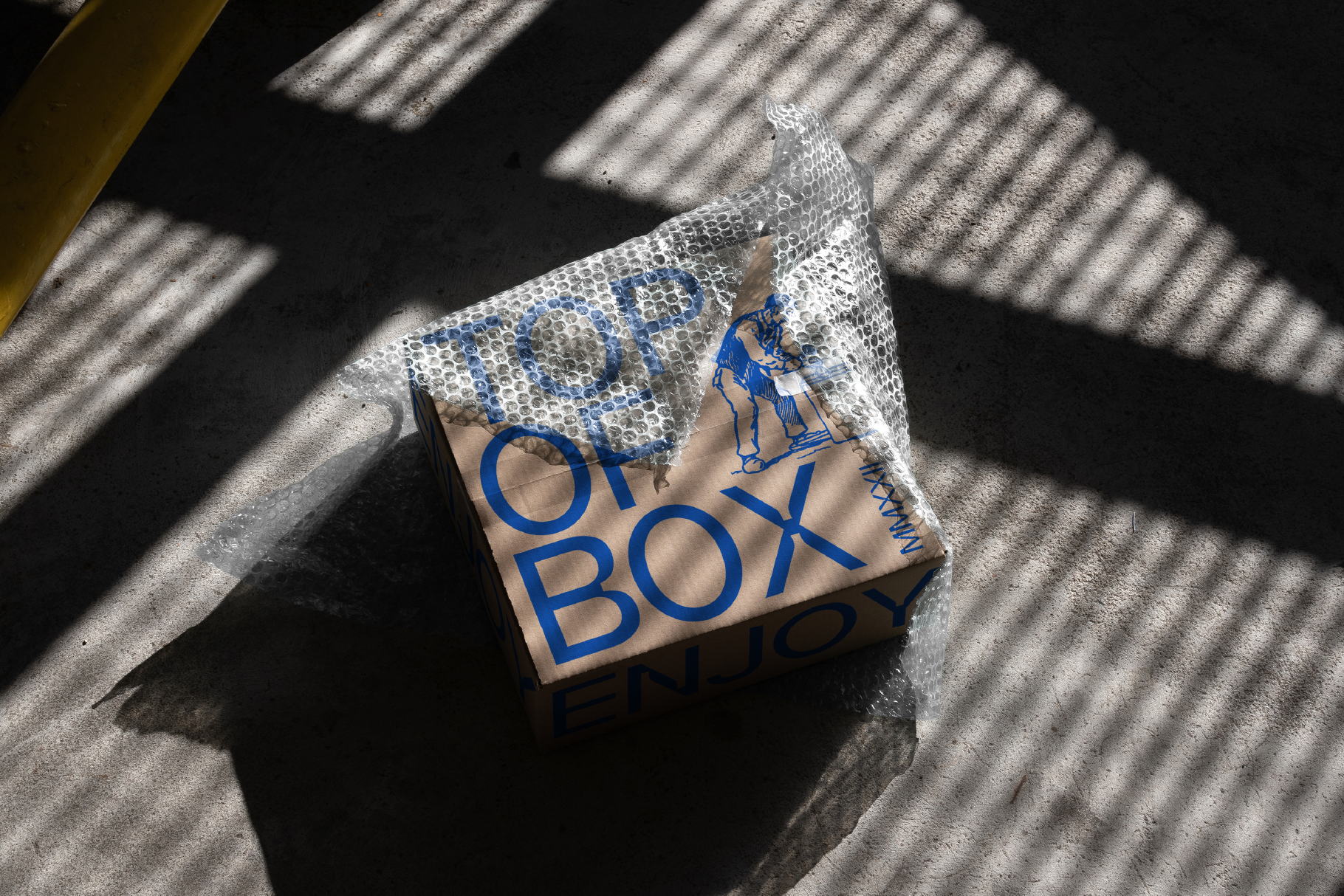 Package mockup in bubble wrap on concrete surface with shadow patterns. Ideal for designers seeking realistic packaging graphics. Box, texture, shadows.