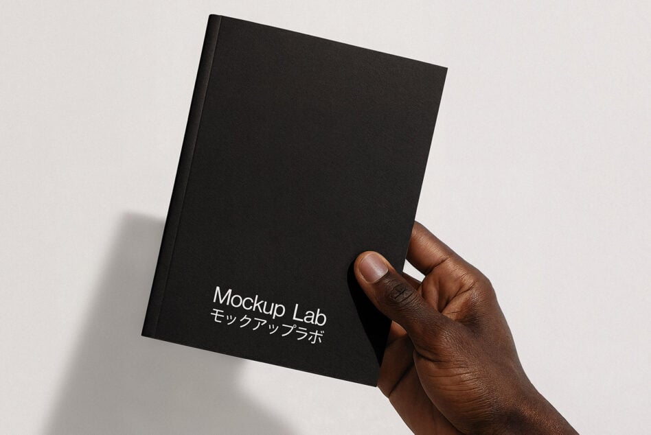 Hand holding black hardcover notebook with white text on spine