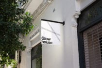 Storefront mockup with Glowhouse logo on a white hanging sign against a building exterior. Ideal for branding mockups, signage design, outdoor advertising.