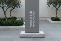Dark gray vertical sign with white text in courtyard with olive trees