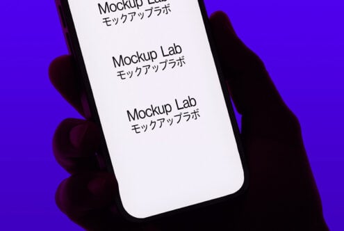 Silhouetted hand holding smartphone with bright white screen on purple