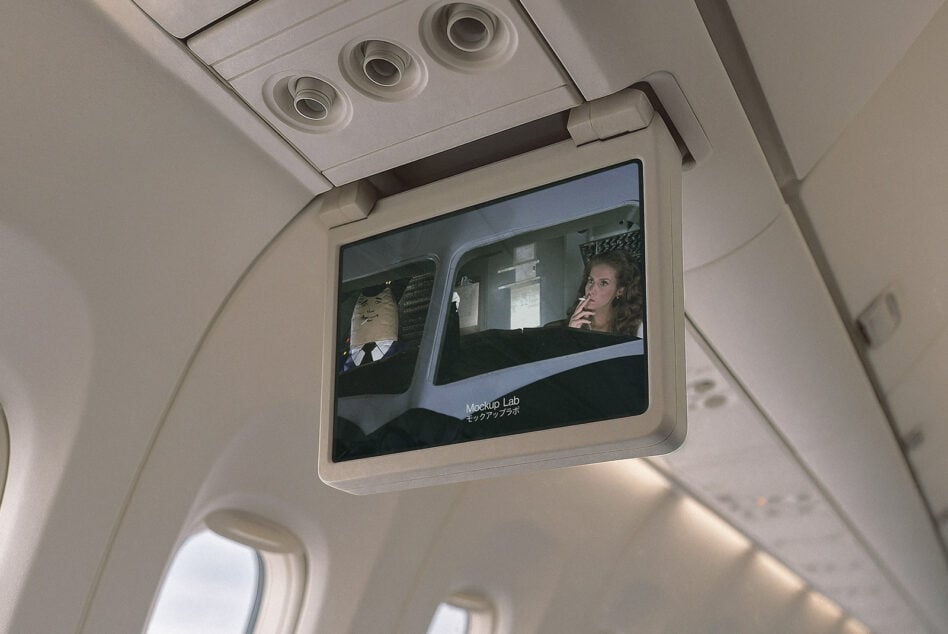 Airplane seatback screen showing video content with cabin overhead vents above
