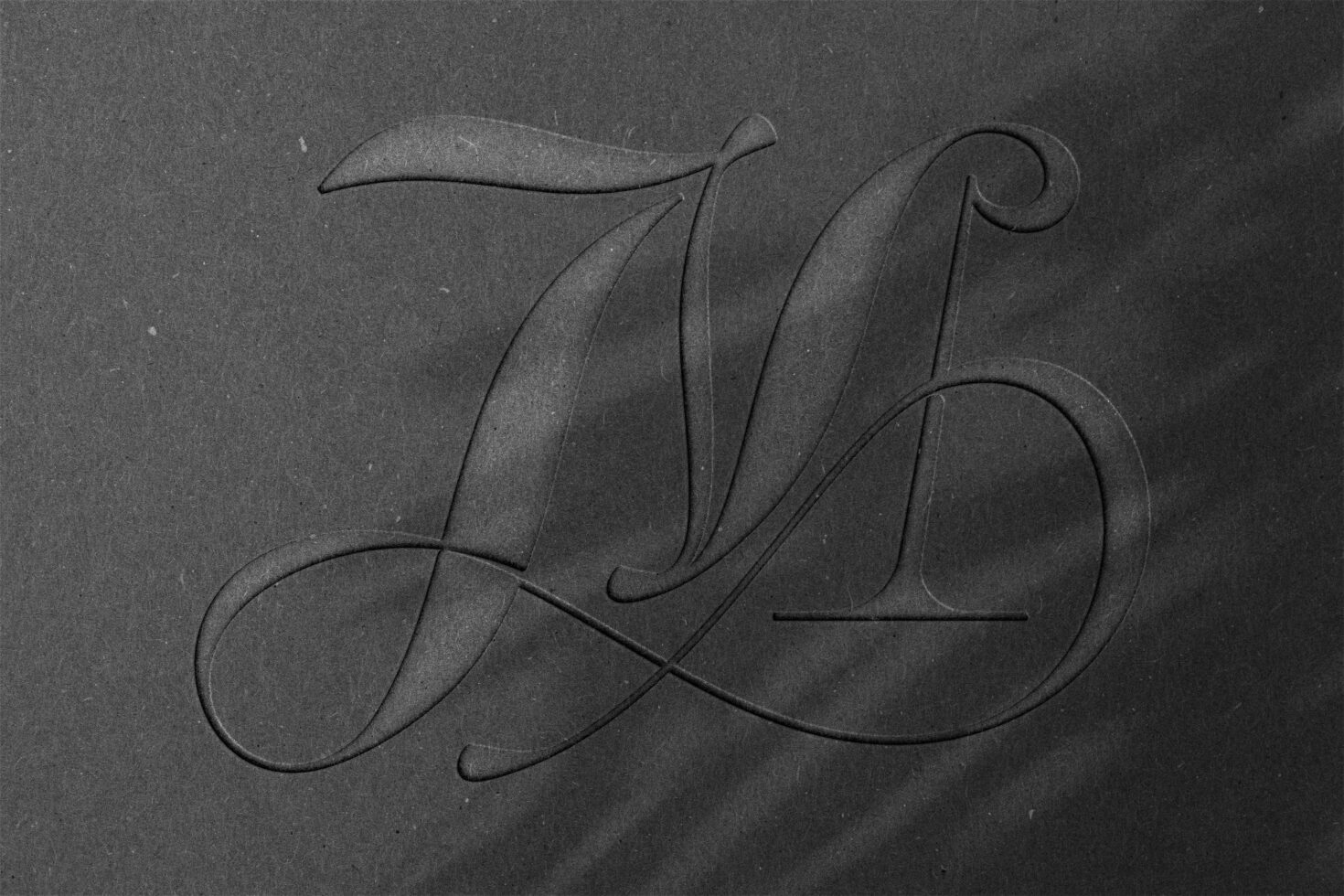 Elegant embossed serif letter monogram on dark textured paper with shadow play perfect for branding mockups or typography design templates.