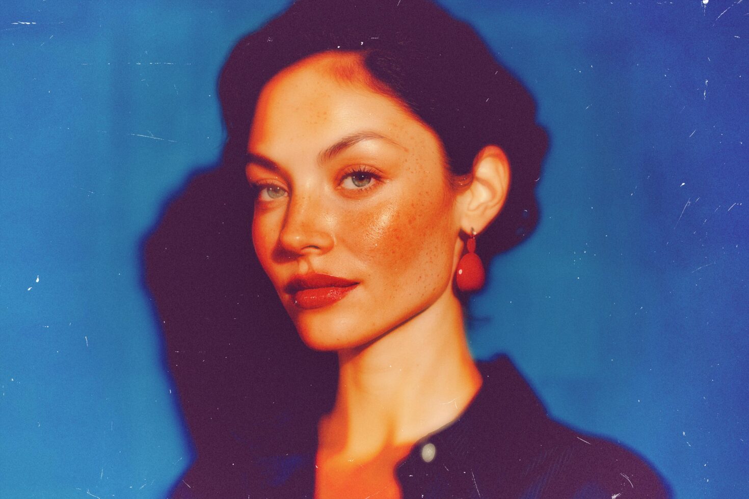 Portrait of a woman with freckles wearing red earrings against a blue background. Ideal for graphics designers. Keywords: portrait, freckles, earrings.