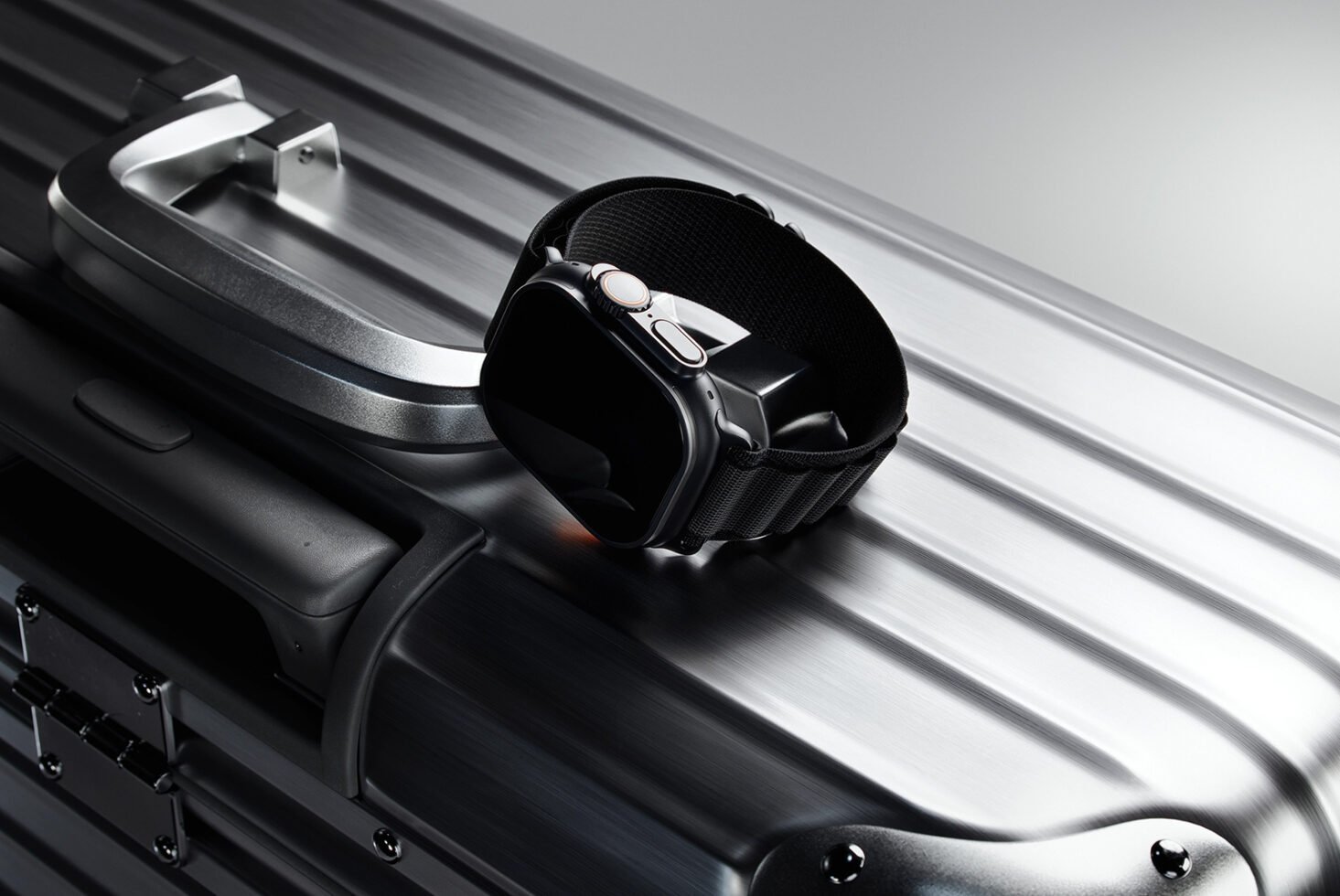 Smartwatch with black band resting on sleek silver suitcase, showcasing modern travel and fashion accessories. Ideal for designer mockups, templates.