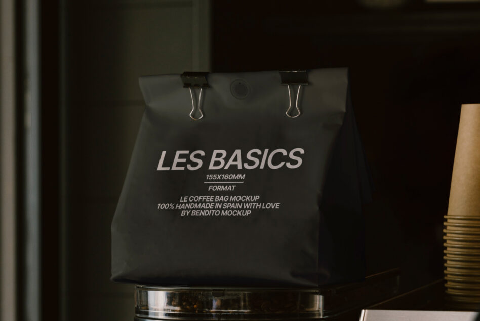 Dark charcoal coffee pouch with metal clips displayed on glossy black container