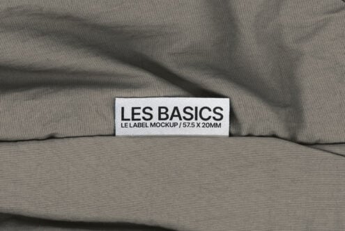Fabric label mockup with Les Basics text on grey textile background, perfect for showcasing clothing branding. Ideal for design and fashion presentations.
