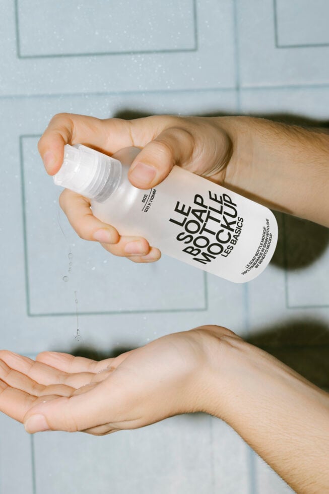 Hand holding white spray bottle dispensing liquid on white tile wall