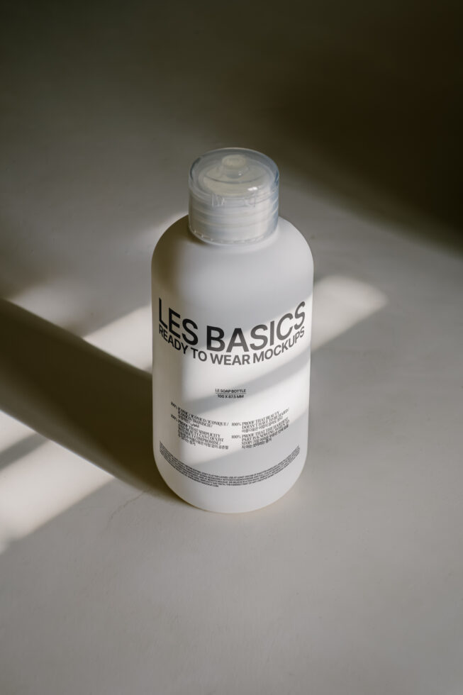 Mockup of a frosted bottle with clear cap on a soft-lit surface labeled Les Basics ready to wear mockups. Ideal for designers seeking product packaging visuals.