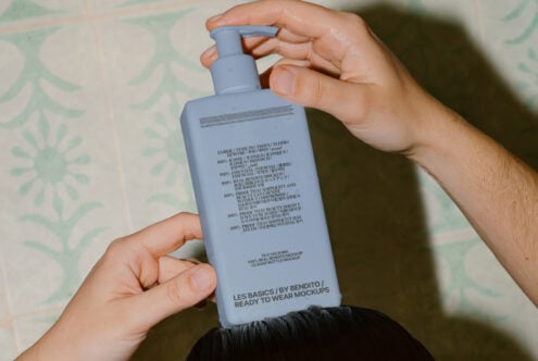 Blue pump bottle held overhead showing full label design on leafy pattern backdrop