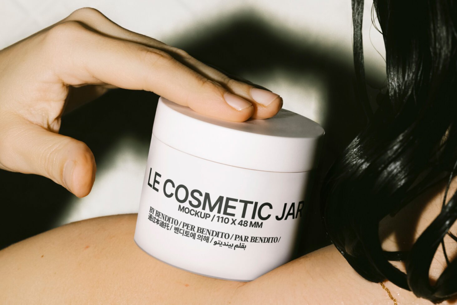 Cosmetic jar mockup features a hand holding a white jar near skin and black hair ideal for beauty product branding packaging design and graphic templates.