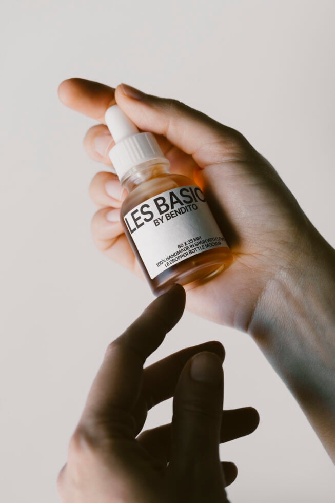 Hand holding a labeled dropper bottle mockup. Ideal for showcasing skincare product designs. Perfect for designers needing high-quality packaging mockups.