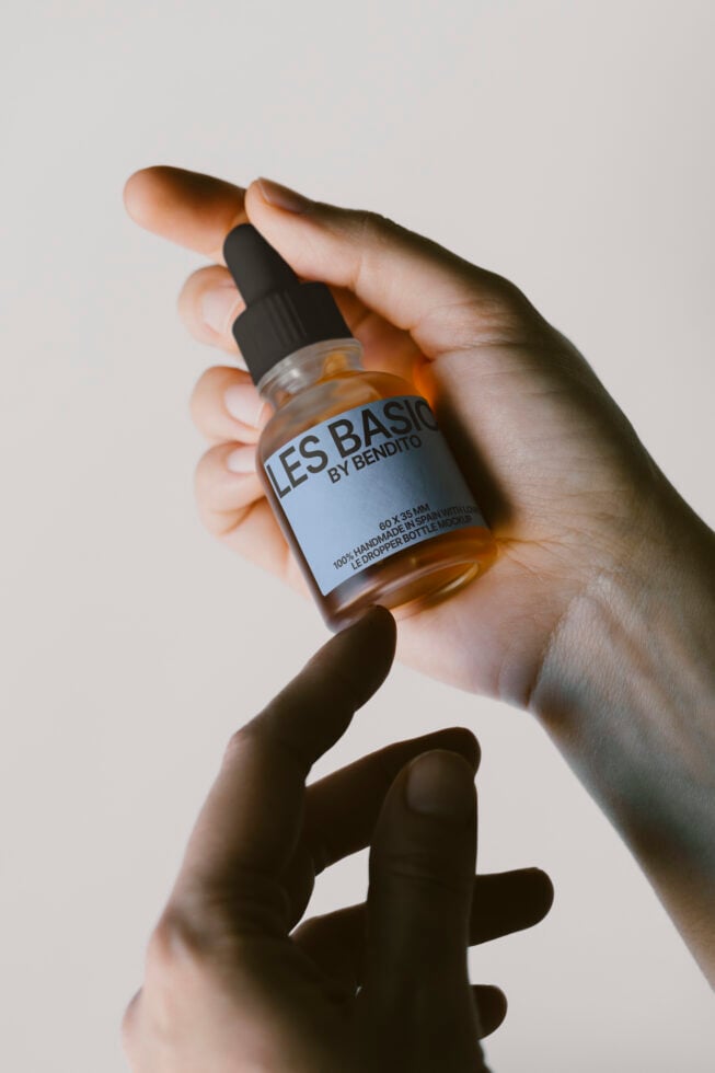 Hand holding a glass dropper bottle labeled Les Basics by Bendito suitable for product mockup design skincare cosmetics minimalist branding.