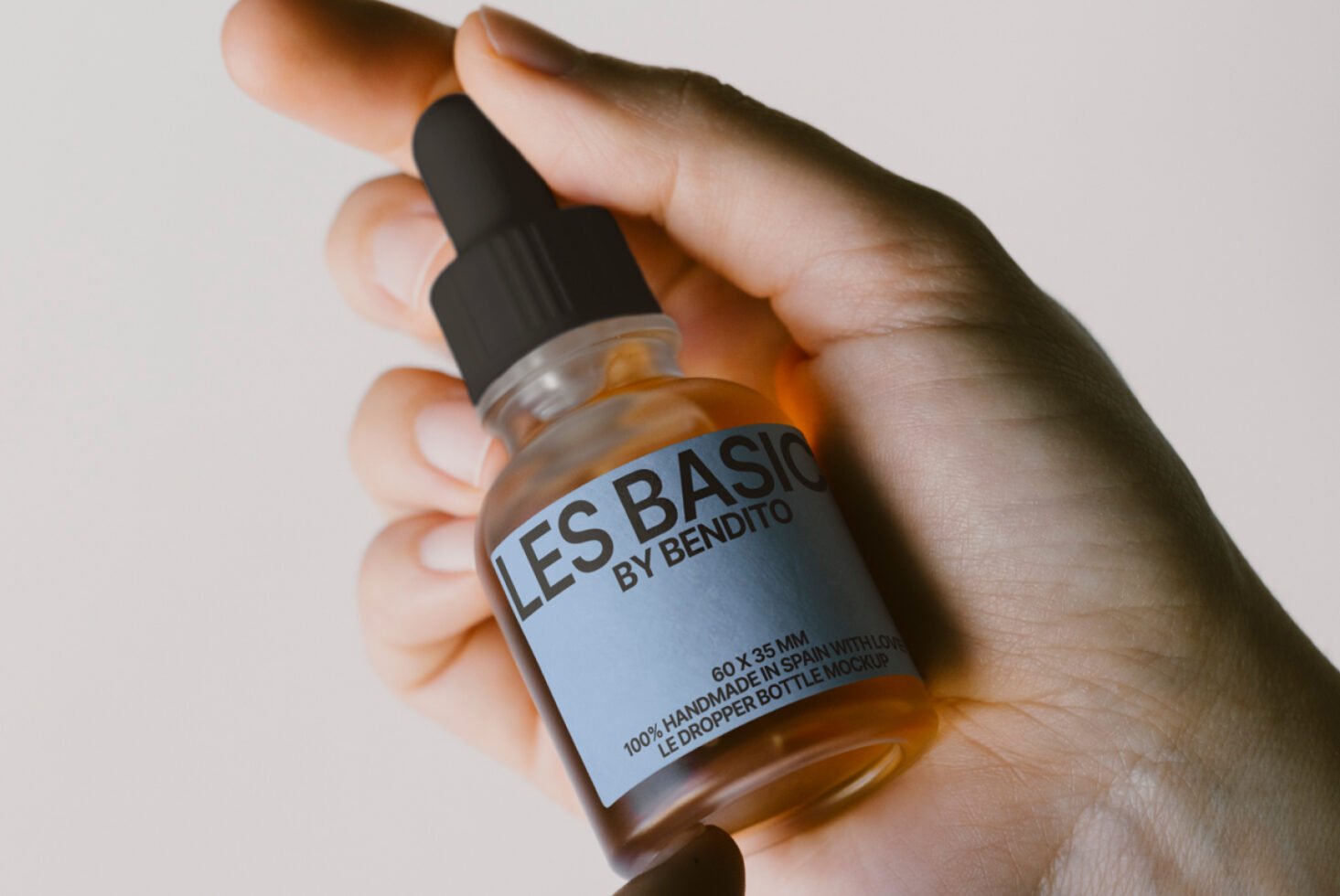 Hand holding a small dropper bottle with a blue labeled design for product mockup. Perfect for designers in need of packaging templates.