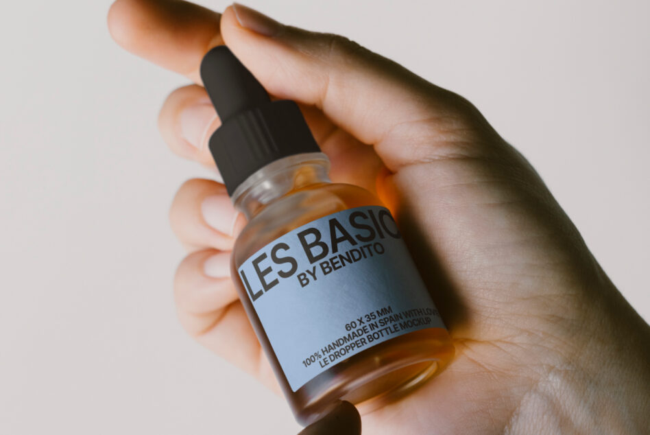 Hands holding amber dropper bottle with black cap displaying Les Basics label mockup