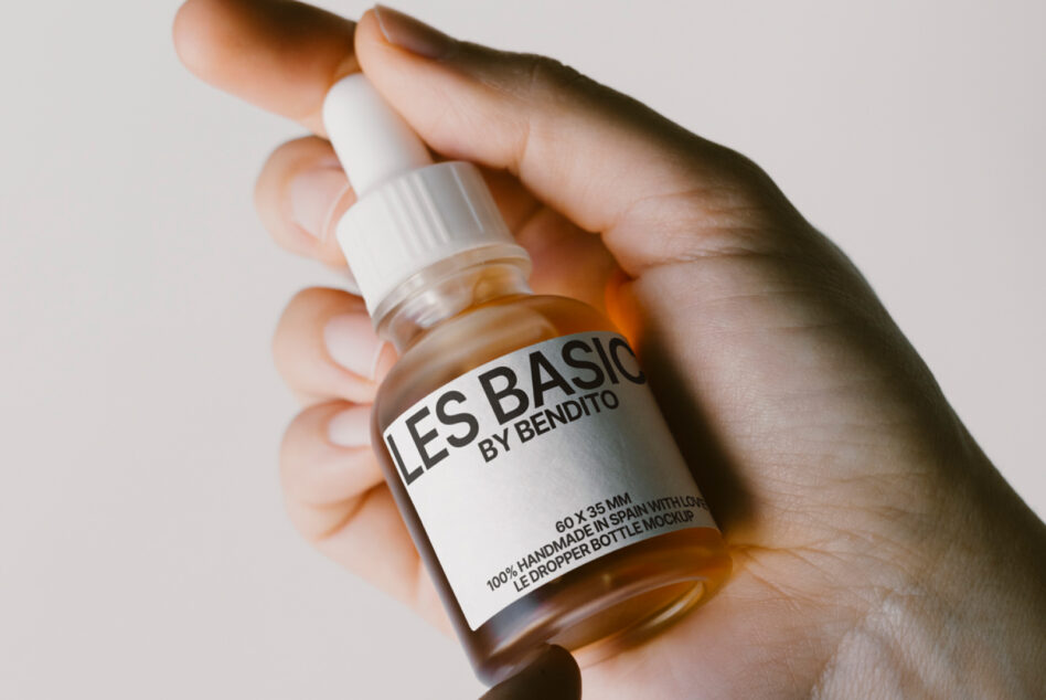 Hands holding amber dropper bottle with white cap showing Les Basics label mockup