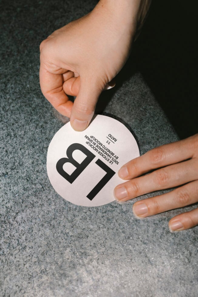 Close-up of hands applying a round sticker mockup on a textured surface perfect for designers needing branding representations for digital assets.