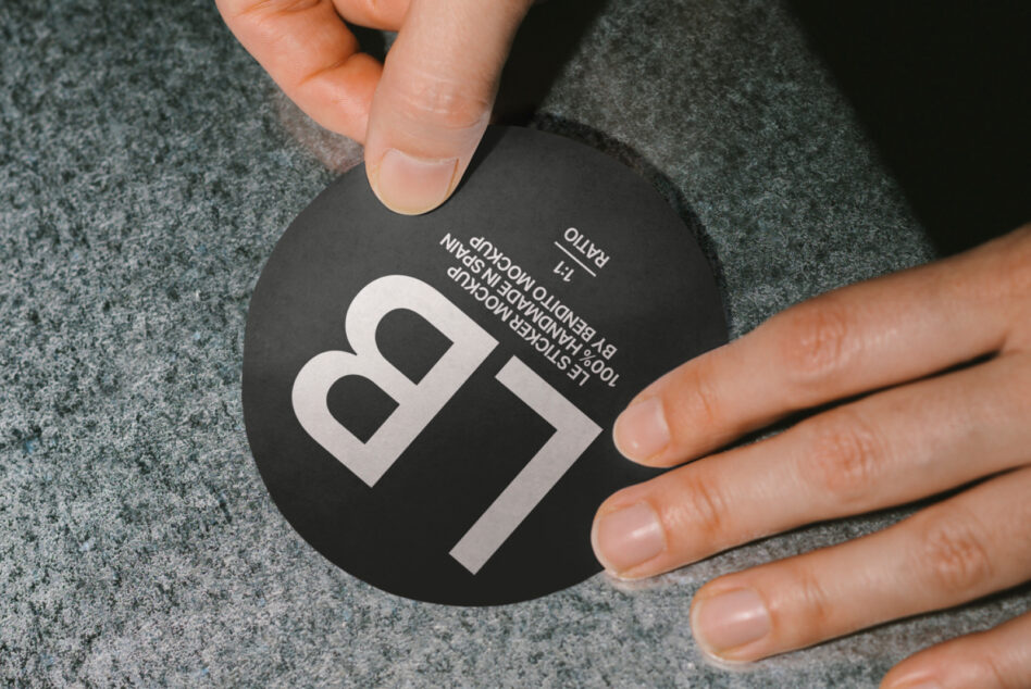 Black circular tag mockup with white logo held in hands on textured surface