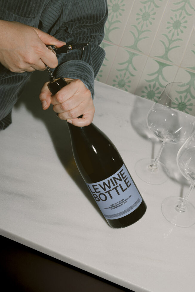 Mockup of hands opening a wine bottle with a corkscrew on a marble surface. Ideal for product presentation, packaging design, and marketing collateral.
