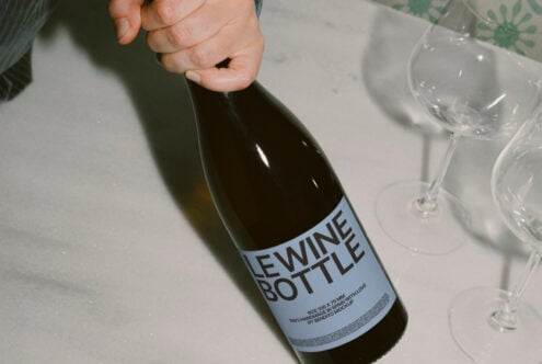 Hand holding wine bottle mockup on marble surface with glasses nearby ideal for designers creating product presentations branding templates graphics