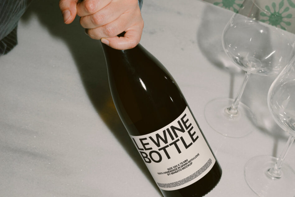 Close up of wine bottle label mockup held in hand with glasses nearby