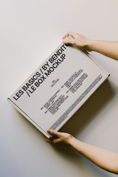 Hands holding cream colored box mockup at angle, front cover visible with typography