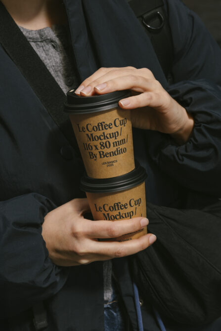 Person holding stacked coffee cups with kraft paper label mockup, black lid, navy blazer