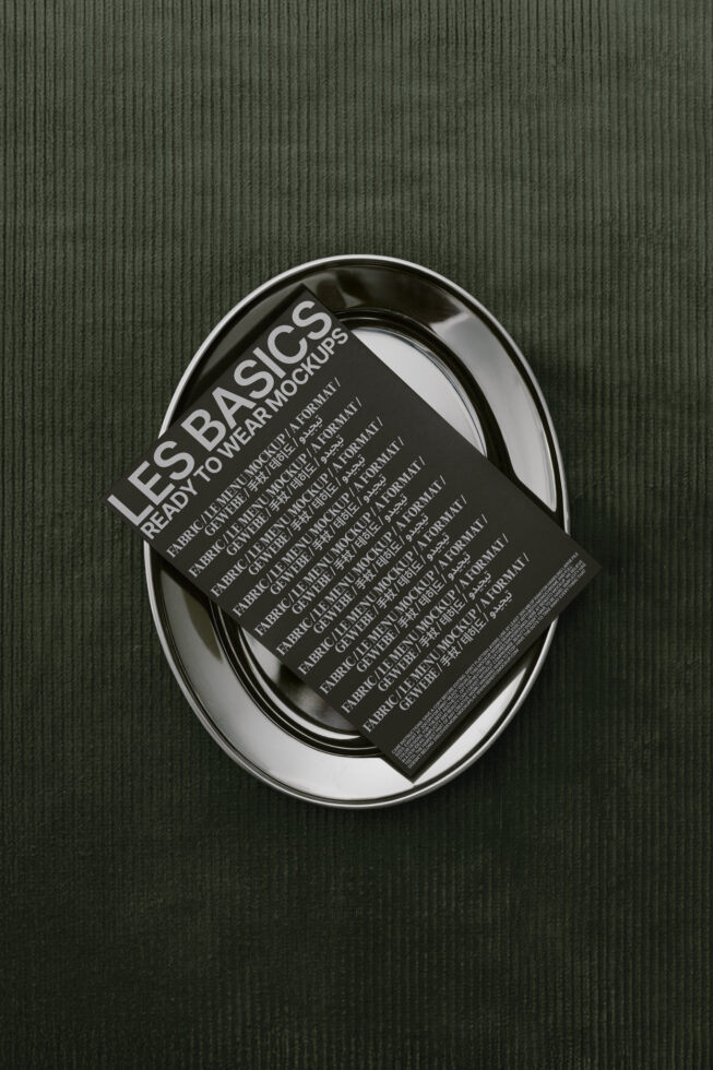 Mockup display of a black card with text tilted on a silver plate over a textured dark green fabric background suitable for designers branding presentations.
