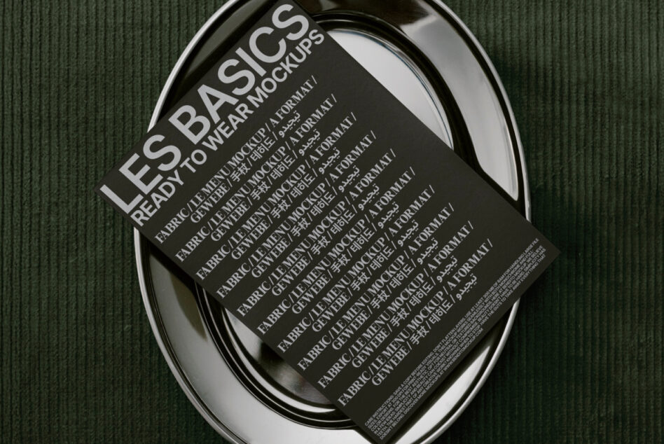 Black ready to wear mockup sheet in oval metal tray on textured green surface