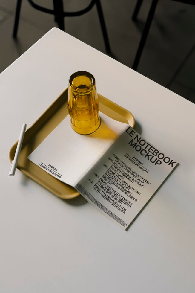 Minimalist notebook mockup on tray with pen and amber glass. Perfect for designers. High-quality graphic template. Modern stationery design.