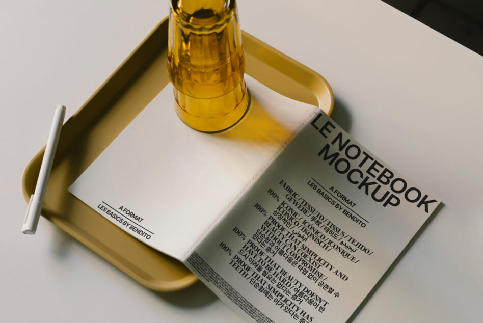 Gold beer bottle with white notebook on brass tray, pen nearby on neutral background