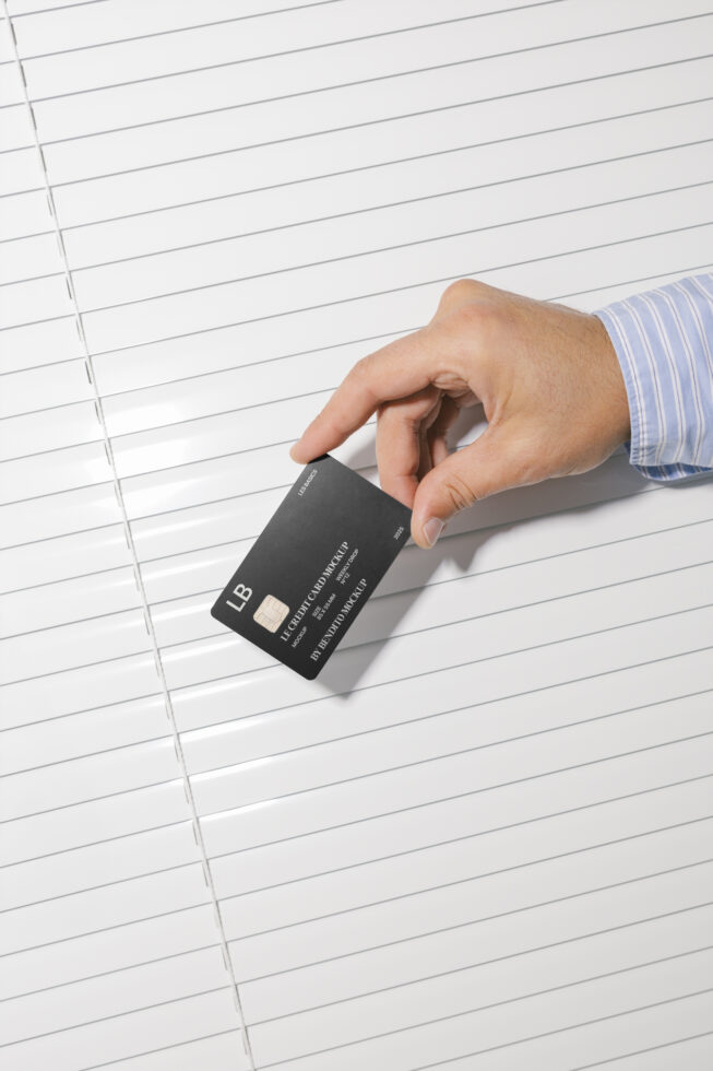 Hand holds a sleek black credit card against white background. Ideal mockup for designers. Keywords: card mockup, business, design resource, branding.