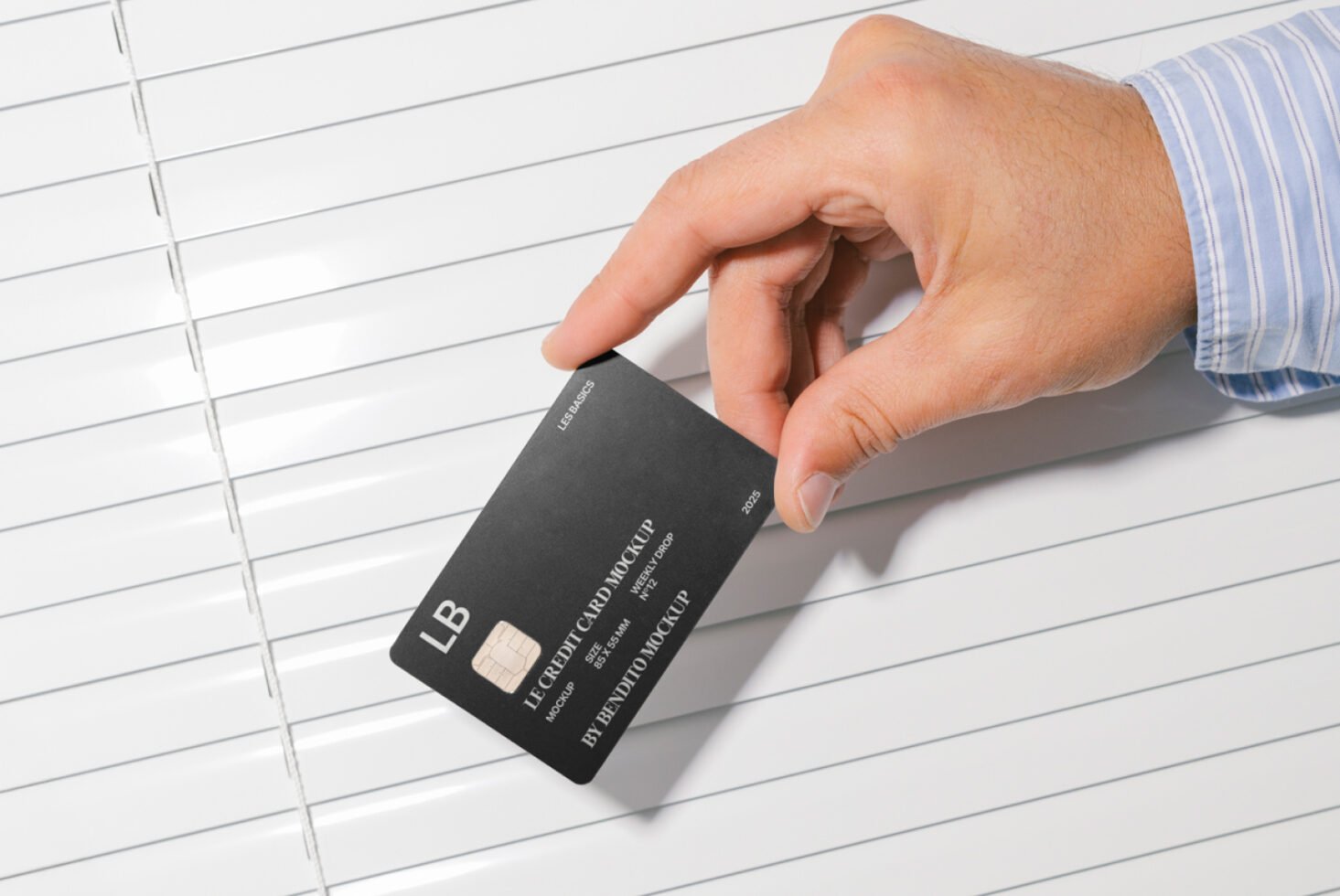 Hand holding black credit card mockup in front of white blinds showcasing design template for designers. Mockups digital assets for designers.