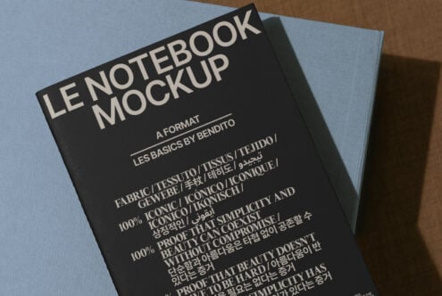 Mockup of a black notebook titled Le Notebook Mockup with multilingual typography placed on a blue surface. Ideal for designers seeking high-quality graphics.
