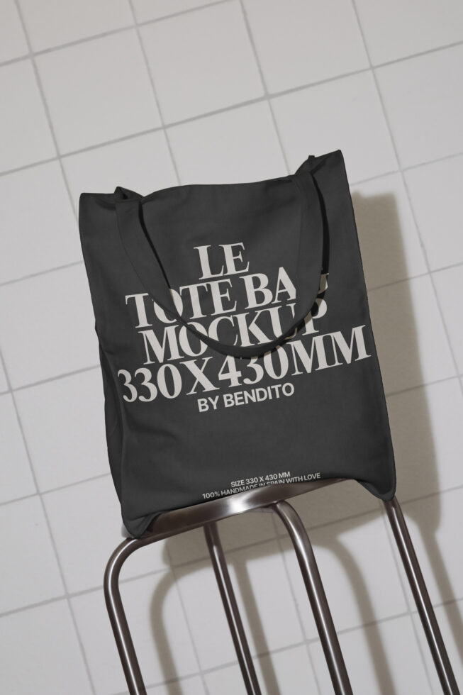 Black tote bag mockup hanging on a chair in a tiled space ideal for showcasing branding or logo designs graphic design mockup high-quality template.