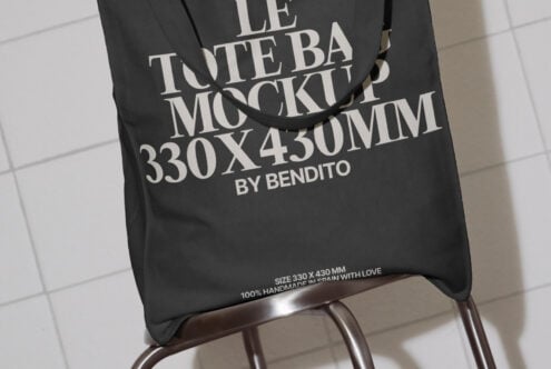 Tote bag mockup featuring a black bag with white text on a chair. Design dimensions 330x430mm. Ideal for showcasing branding, logo, or graphic designs.
