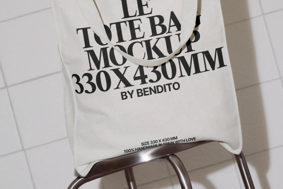 Cream cotton tote bag mockup draped on metal chair leg, neutral tiled background