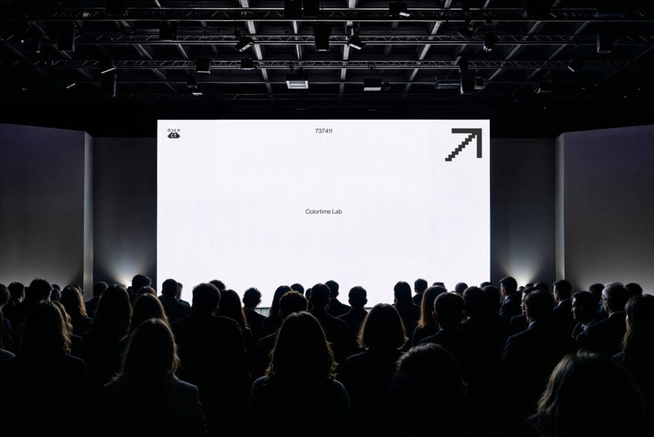 Crowd watching projection screen displaying white background with minimal branding