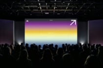 Crowd viewing vibrant gradient projection from purple through yellow to blue