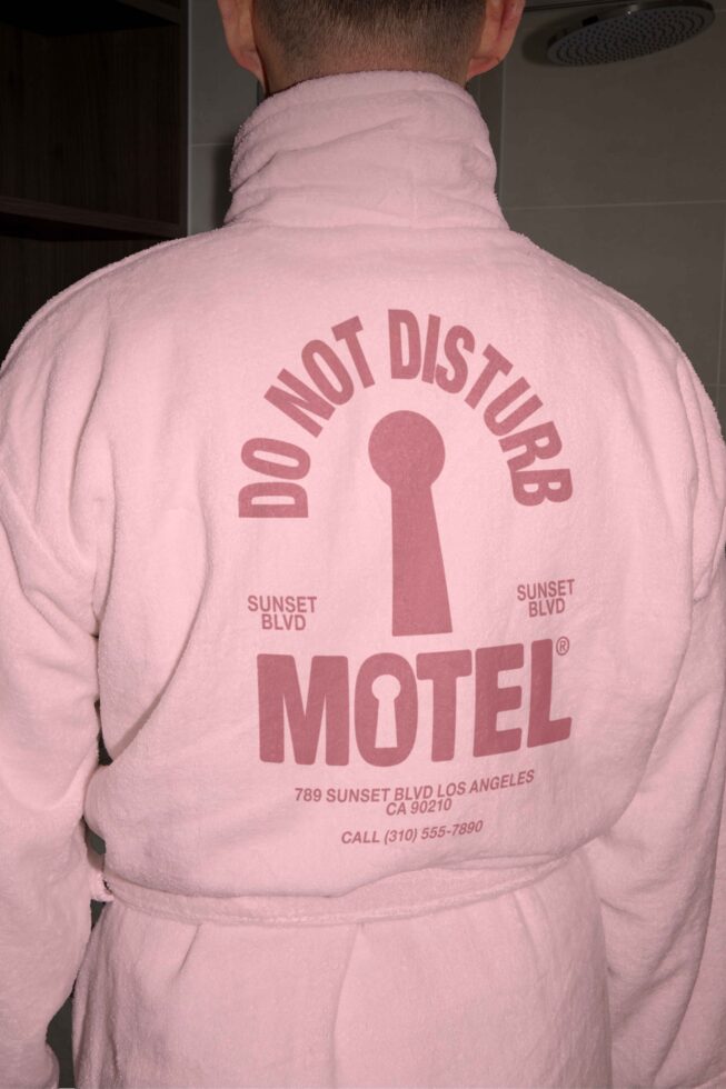 Person wearing pink bathrobe with Do Not Disturb Motel graphic design Sunset Blvd text, suitable for designers looking for trendy graphics or mockups.