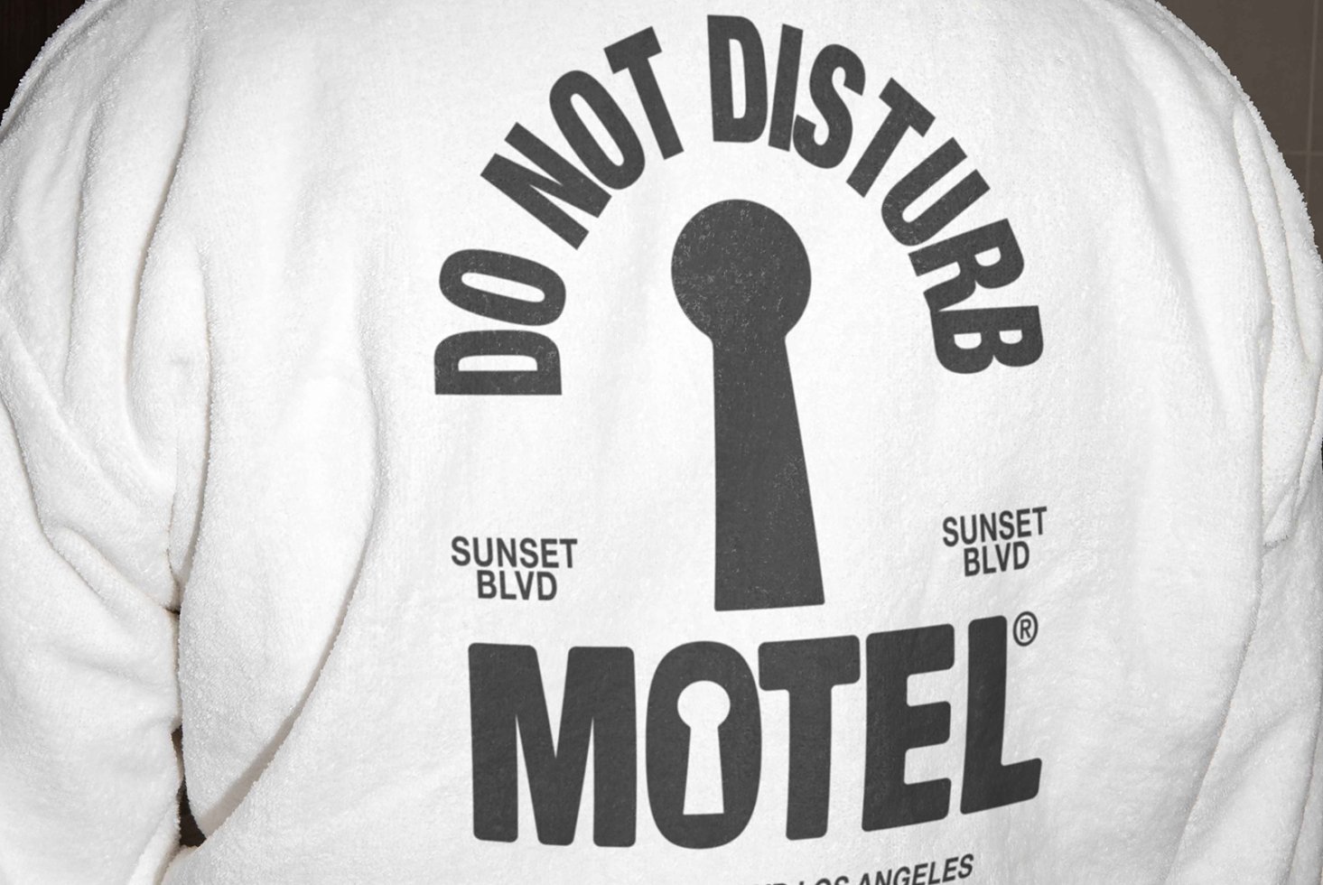 Back of white robe featuring bold graphic text do not disturb motel with keyhole design and Sunset Blvd. Perfect for graphics or typography inspiration.