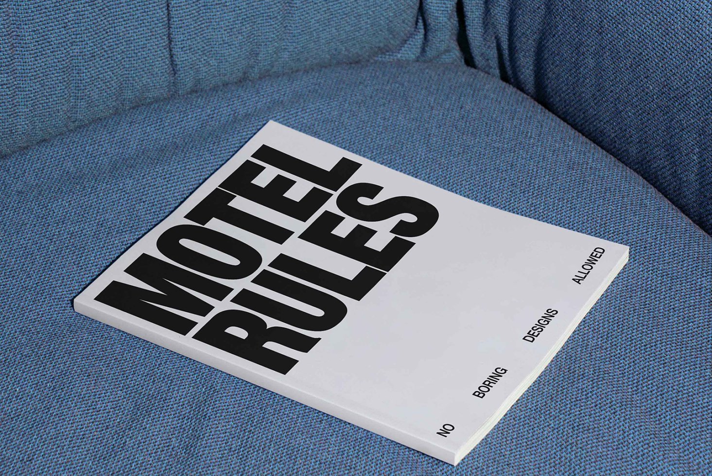 Magazine with bold text Motel Rules on a blue fabric background. Ideal for graphic designers seeking layout inspiration or typography mockups.