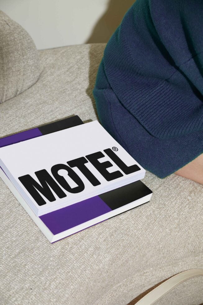 Modern graphic design book on a beige couch featuring bold lettered title Motel in black and purple colors for creative inspiration and design projects.