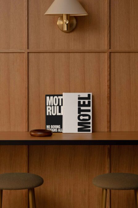 Square hardcover book mockup in black on wooden shelf with brass sconce