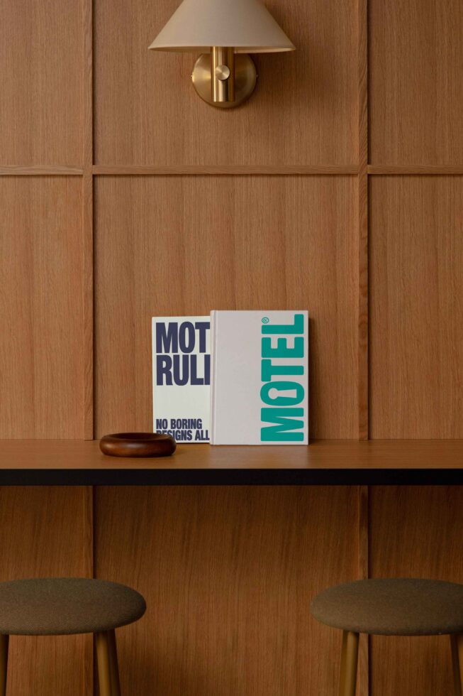 Wooden interior with wall lamp, stools, and a shelf displaying two books with bold typography. Ideal for design mockups and interior design themes.