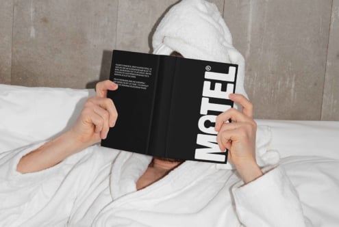 Person relaxing in bed with towel on head reading black book with bold text Motel great for designers mockups cozy lifestyle reading relaxation SEO