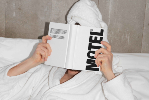 Person in a robe on a bed reading a book with bold text Motel. Perfect for design inspiration mockup graphic design lifestyle cozy SEO keywords.